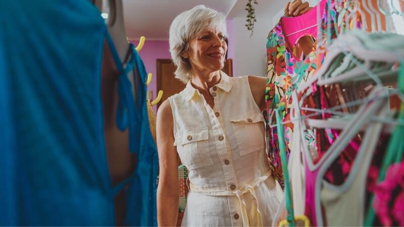 Tendências de Moda Verão 2026: peças Hiroshima, LARC e Narval que prometem vender o ano todo 1 Mulher representando uma consultora de moda, segurando peça vibrante de cores tropicais, em meio a roupas de verão com padrões coloridos, refletindo as tendências para o verão 2026